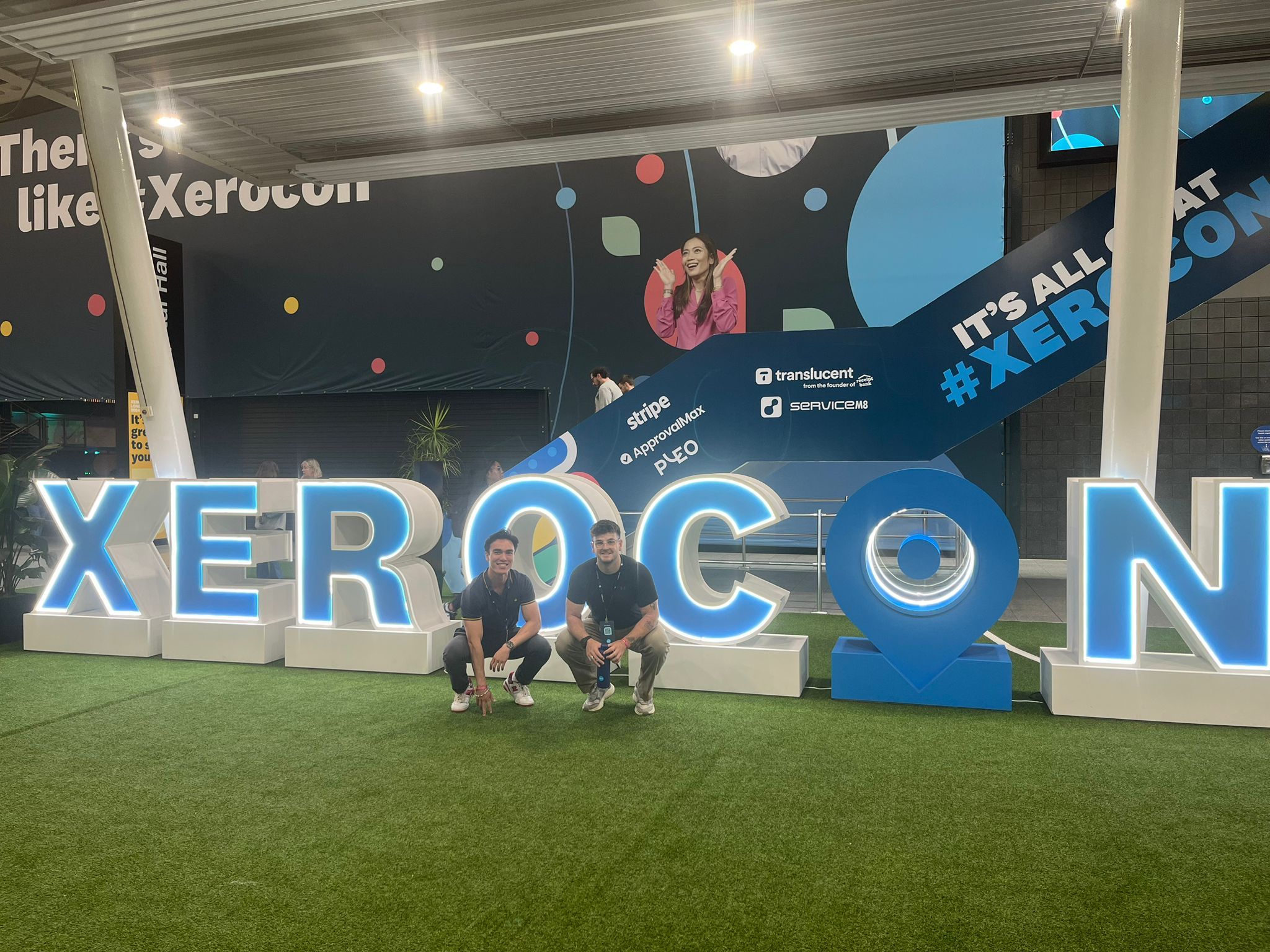 Description: Xerocon 2024. Photo showing Patrick and Harvey crouching in front of a Xerocon sign